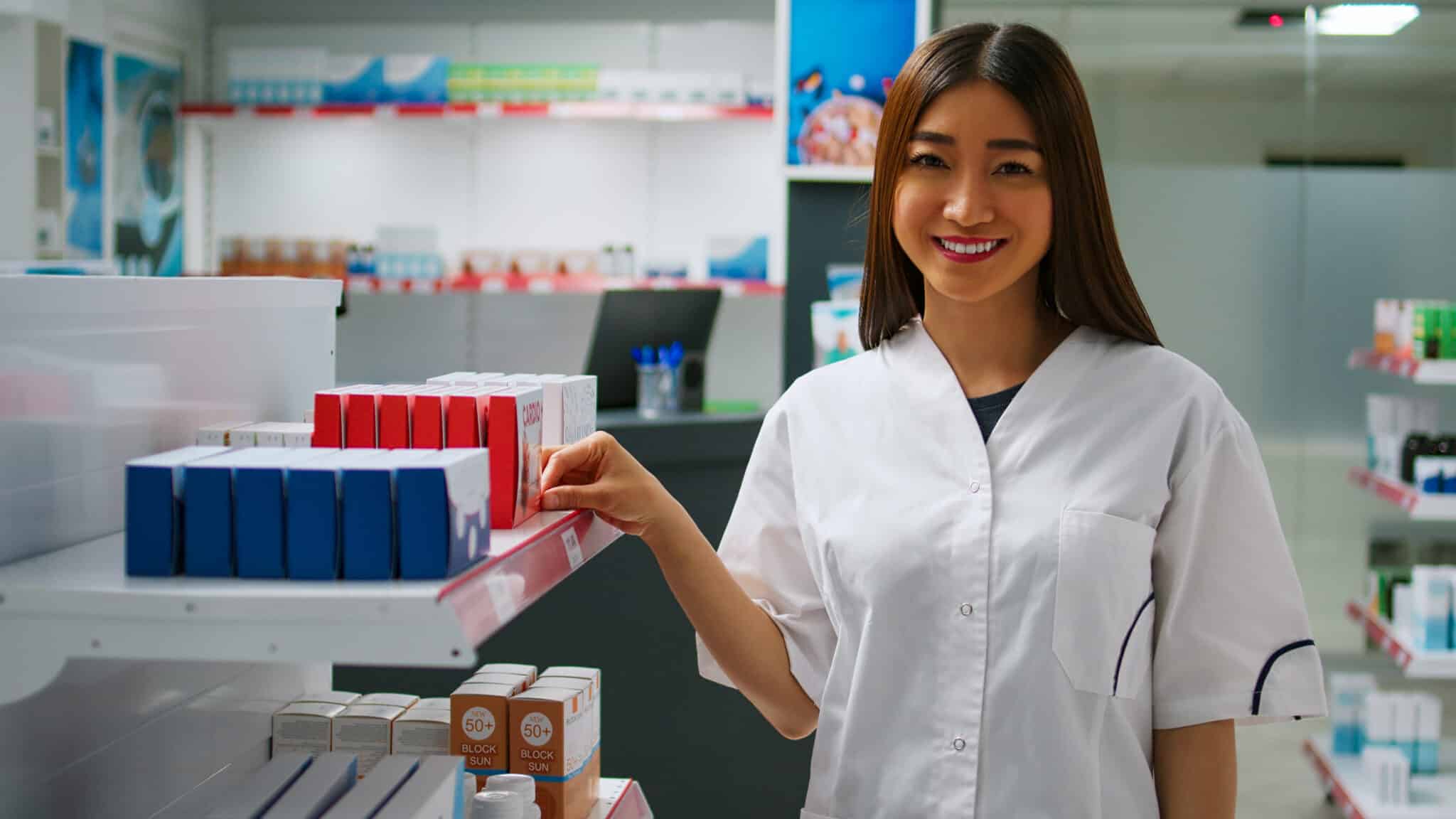 Pharmacy professional smiling while organizing medicine boxes on shelves, exemplifying mental well-being in the workplace.